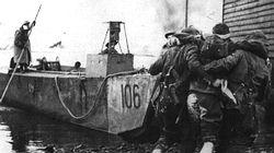 A wounded British commando is helped to a landing craft as victorious troops leave Vaagso with 100 German prisoners.